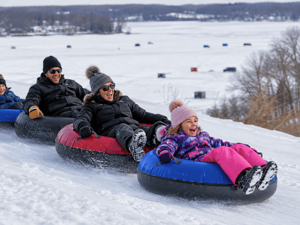 A family enjoying Okoboji winter activities while snow tubing on a hill overlooking the frozen Iowa Great Lakes.