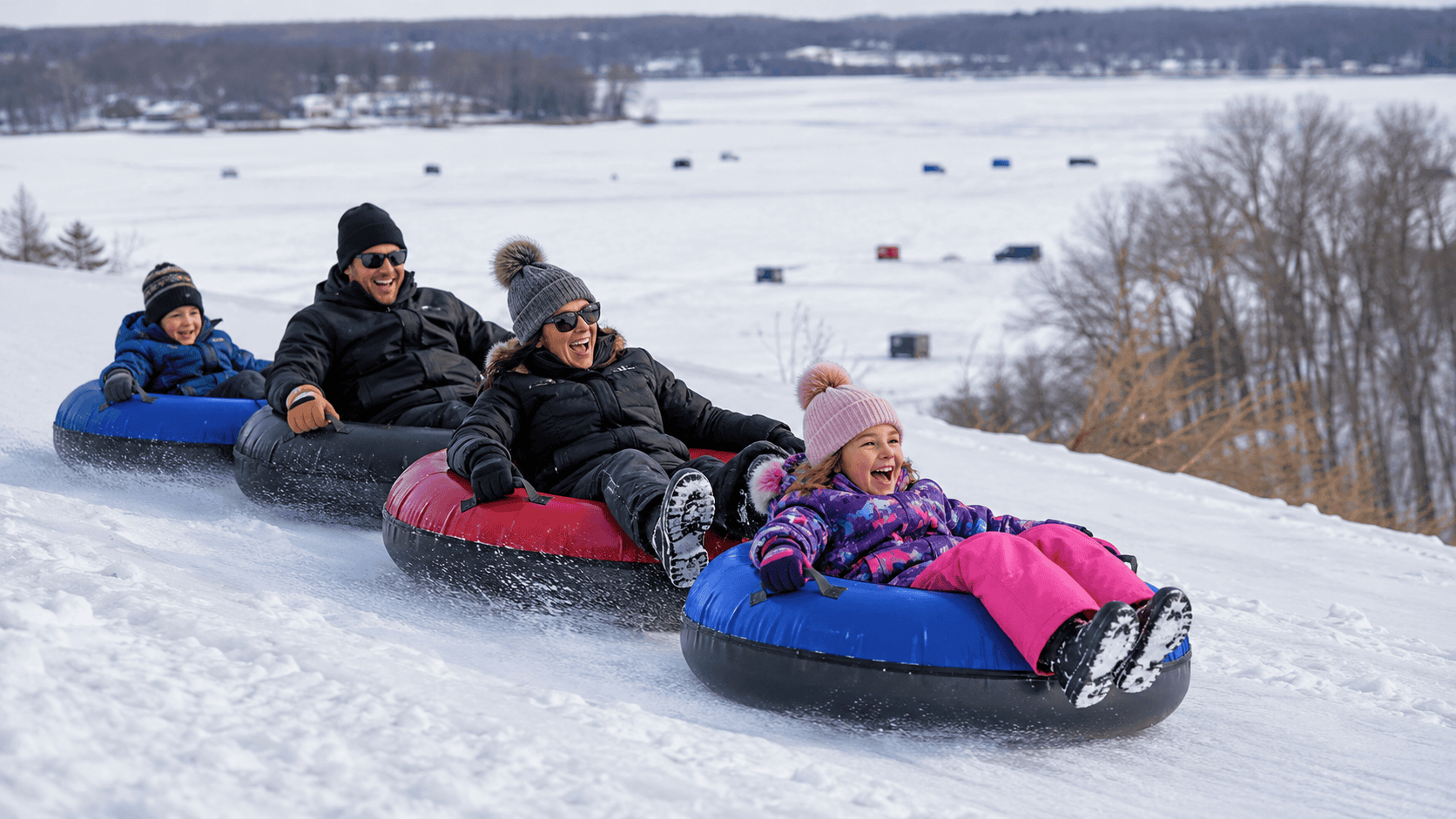 A family enjoying Okoboji winter activities while snow tubing on a hill overlooking the frozen Iowa Great Lakes.