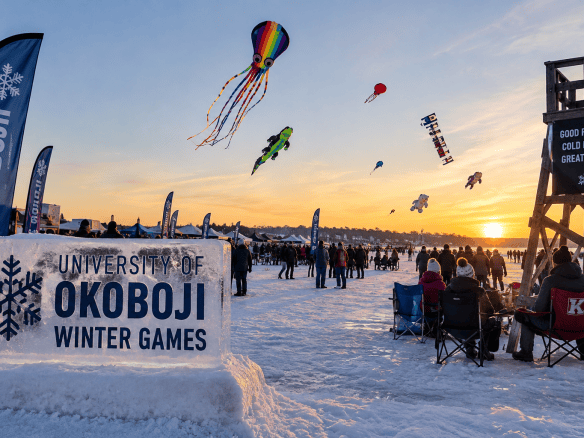 Colorful kites flying above a frozen lake as bundled-up visitors enjoy the Okoboji Winter Games.