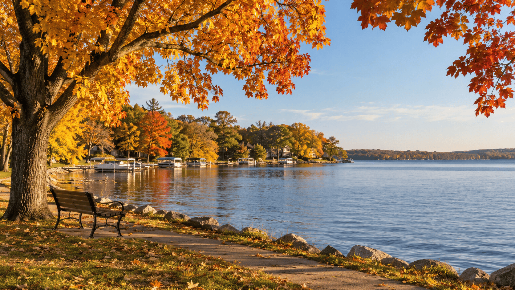 Okoboji fall colors surrounding a quiet lakeside bench, with golden autumn trees, docks, and calm water.